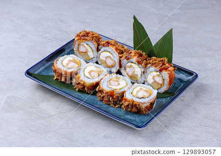 Crispy sushi rolls filled with shrimp, cream cheese, and egg, topped with fried onions and sweet sauce, served on a blue ceramic plate. Crispy sushi rolls filled with shrimp, cream cheese, and egg, topped with fried onions and sweet sauce, served on a blue ceramic plate. 129893057