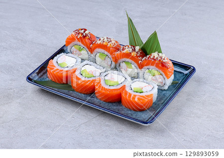 Fresh salmon sushi rolls with avocado, cream cheese, and shrimp, artfully arranged on a blue plate with garnish and green leaves. Fresh salmon sushi rolls with avocado, cream cheese, and shrimp, artfully arranged on a blue plate with garnish and green leaves. 129893059