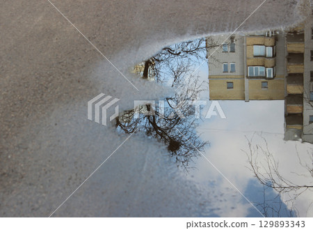 Puddle on asphalt with reflection of high-rise buildings and trees 129893343