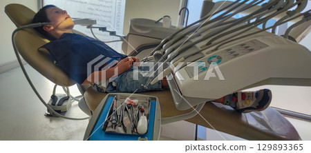 Child in dental clinic lying in chair with professional dental instruments in foreground. preventive dental measures, pediatric dental implantation, health care, hygiene, pediatric dentistry Child in dental clinic lying in chair with professional dental instruments in foreground. preventive dental measures, pediatric dental implantation, health care, hygiene, pediatric dentistry 129893365