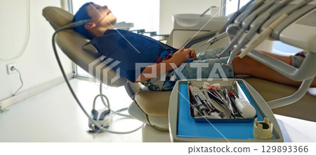 Child in dental clinic lying in chair with professional dental instruments in foreground. preventive dental measures, pediatric dental implantation, health care, hygiene, pediatric dentistry Child in dental clinic lying in chair with professional dental instruments in foreground. preventive dental measures, pediatric dental implantation, health care, hygiene, pediatric dentistry 129893366