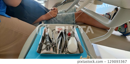 Child in dental clinic lying in chair with professional dental instruments in foreground. preventive dental measures, pediatric dental implantation, health care, hygiene, pediatric dentistry 129893367