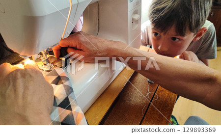 Child watching sewing on machine - DIY crafting, family bonding, handmade textiles, slow living home studio, sustainable fashion learning moment 129893369