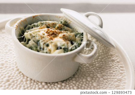 Delicious baked dish, topped with melted cheese and seasonings, served in a white ceramic pot with a lid. Baked green asparagus beans. Delicious baked dish, topped with melted cheese and seasonings, served in a white ceramic pot with a lid. Baked green asparagus beans. 129893473