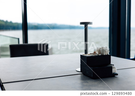 A modern cafe scene by the lake, a minimalist table setting and natural light. A minimalist table setting by a large window with a serene lake view in the background. The scene evokes a sense of calm 129893480