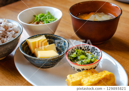 A Japanese-style breakfast set featuring mixed grain rice, miso soup, tamagoyaki (rolled egg), and a small side dish. A Japanese-style breakfast set featuring mixed grain rice, miso soup, tamagoyaki (rolled egg), and a small side dish. 129893821