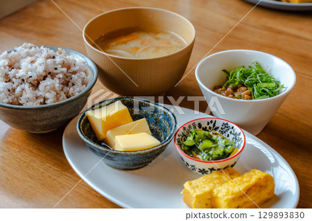 A Japanese-style breakfast set featuring mixed grain rice, miso soup, tamagoyaki (rolled egg), and a small side dish. 129893830