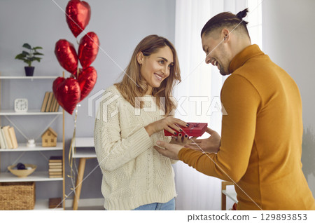 Man holding red present box and congratulating pretty woman on holiday standing at home. Man holding red present box and congratulating pretty woman on holiday standing at home. 129893853