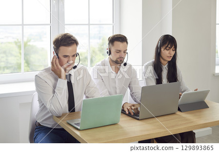Support operators with headsets on laptops and tablet at hotline helpdesk team 129893865