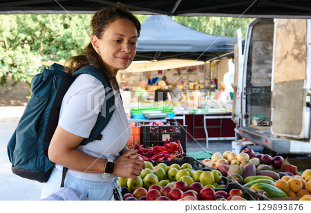 A woman explores a vibrant outdoor market, browsing fresh produce including fruits and vegetables, showcasing healthy living and sustainable food options. A woman explores a vibrant outdoor market, browsing fresh produce including fruits and vegetables, showcasing healthy living and sustainable food options. 129893876