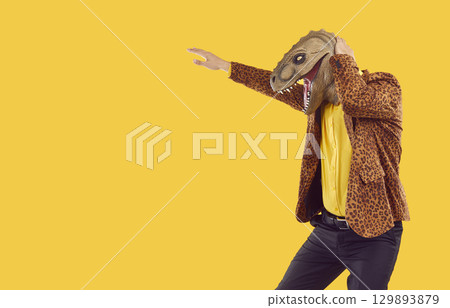 Man in leopard jacket and dinosaur mask dancing isolated on yellow copy space background Man in leopard jacket and dinosaur mask dancing isolated on yellow copy space background 129893879