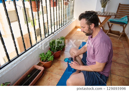 A serene moment of a man practicing mindfulness and relaxation on his home balcony. The image conveys harmony, health, and tranquility, with an urban backdrop and focus on self-care. 129893996