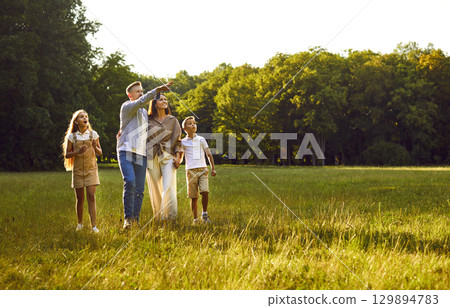 Happy mom, dad and children looking up at sky while walking in green park in summer Happy mom, dad and children looking up at sky while walking in green park in summer 129894783