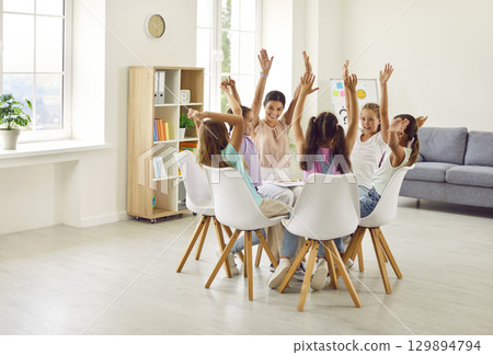Group of school children girls sitting in a circle with psychologist and raising hands up. 129894794