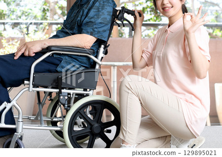 An elderly man in a wheelchair and a young female caregiver 129895021