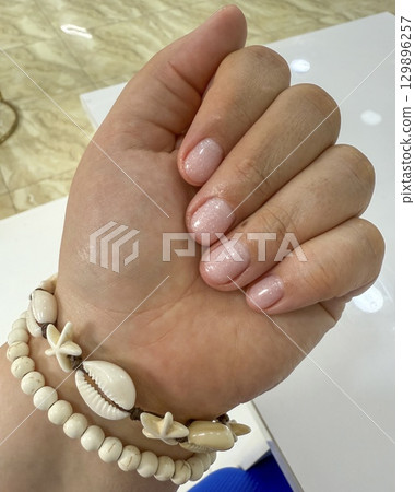 Female hand with pink manicure and seashell bracelet Female hand with pink manicure and seashell bracelet 129896257