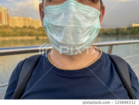 Close-up of man wearing medical mask outdoors near river Close-up of man wearing medical mask outdoors near river 129896312
