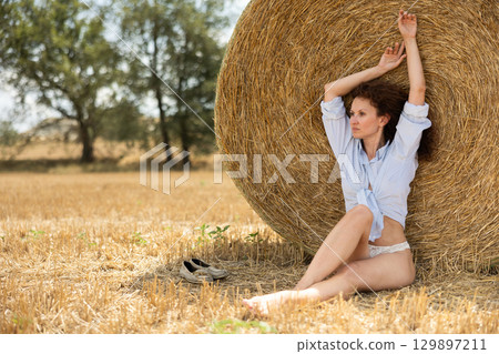 Woman in shirt and panties sits near haystack Woman in shirt and panties sits near haystack 129897211