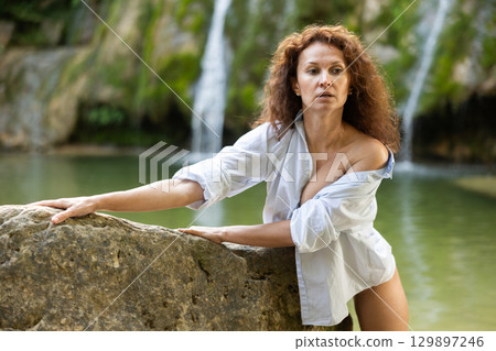 Portrait of half-naked woman in white shirt and white panties against the background of tropical waterfall 129897246