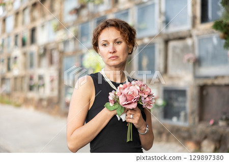 Sorrowful woman in black standing in cemetery with flowers Sorrowful woman in black standing in cemetery with flowers 129897380