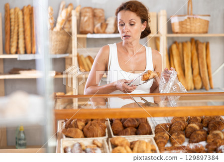 Woman in casual clothes chooses hot croissants for breakfast in bakery Woman in casual clothes chooses hot croissants for breakfast in bakery 129897384