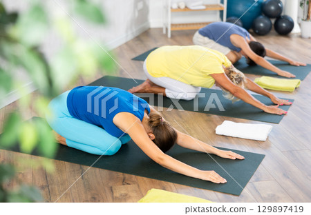 Middle-aged woman practicing child's pose of yoga in light fitness room 129897419