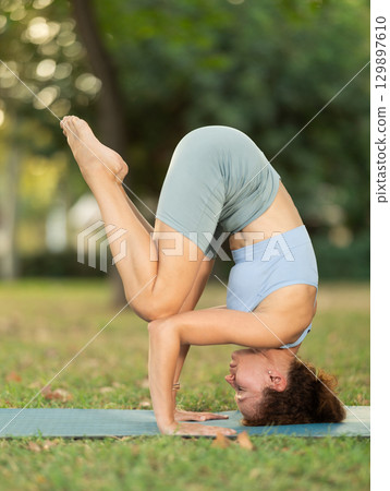 Meditation in a summer park - woman standing on her head while doing yoga in garden Meditation in a summer park - woman standing on her head while doing yoga in garden 129897610