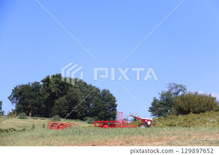 A rural mountain landscape with a blue sky and a red farm car parked on a hill 129897652