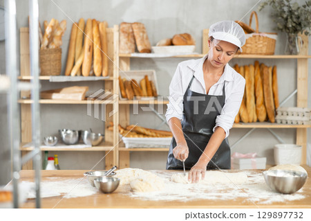 Female baker cutting raw dough with knife to make croissants or buns Female baker cutting raw dough with knife to make croissants or buns 129897732
