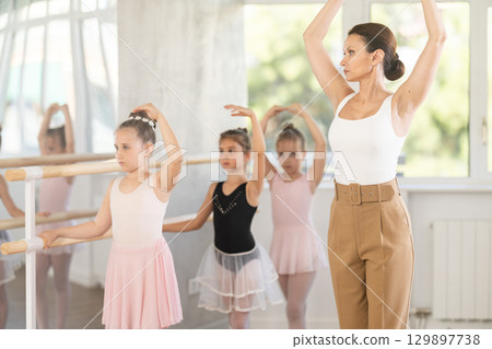 Girl students of choreographic school look at woman teacher and repeat movements after her Girl students of choreographic school look at woman teacher and repeat movements after her 129897738