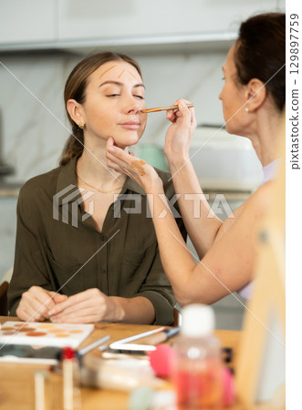 Woman doing contour makeup to relaxed female friend at home Woman doing contour makeup to relaxed female friend at home 129897759