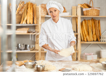 Professional female baker preparing pizza dough in bakery 129897762