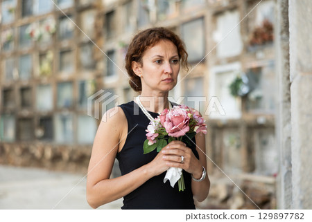 Drieving woman in black dress standing with bouquet by columbarium Drieving woman in black dress standing with bouquet by columbarium 129897782