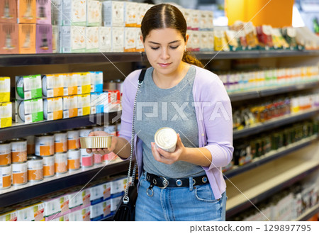 Young cheerful woman buying canned pet food in pet store Young cheerful woman buying canned pet food in pet store 129897795