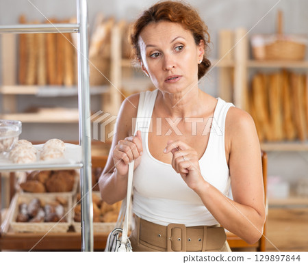 Young European woman near window of bakery food court store examines assortment 129897844