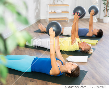 Mom, grandmother and teen grandson performing exercises with softball lying on floor 129897908