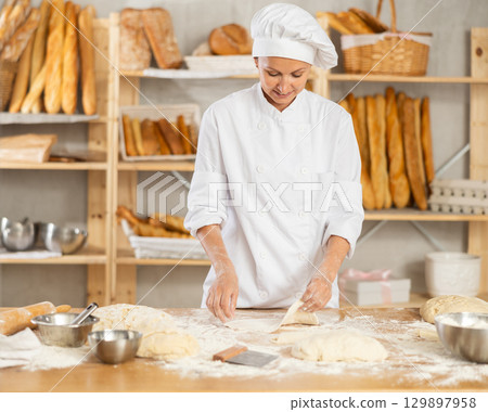 Professional female baker preparing pizza dough in bakery 129897958