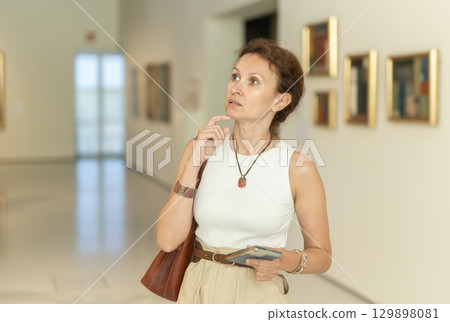 Positive woman visitor with smartphone in hands exploring religious art in museum 129898081