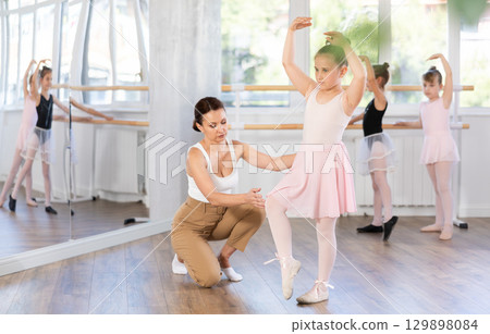 In studio, mentor corrects girls arm and leg, teaches correct dynamics and execution of movements 129898084