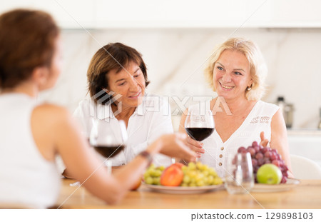 Girlfriends chatting and drinking wine at home party table 129898103