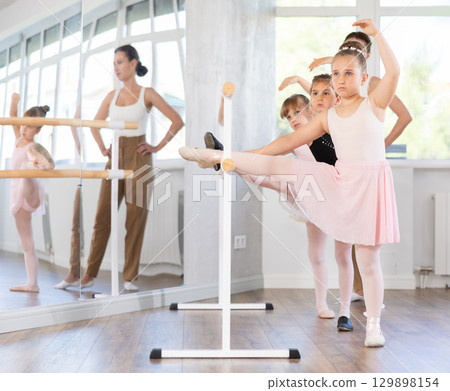 Ballet pose grand batman - little girls at a choreography lesson are learning ballet movements in studio Ballet pose grand batman - little girls at a choreography lesson are learning ballet movements in studio 129898154