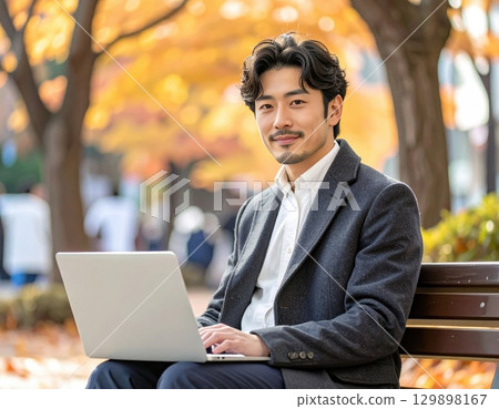 Man using laptop on park bench 129898167