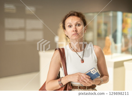 Woman with phone looking around in museum hall 129898211