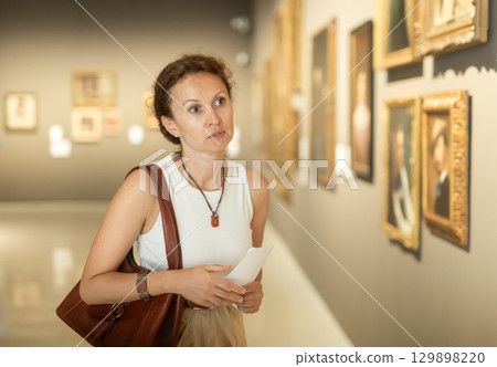 Interested woman in casual clothes exploring paintings in halls of museum 129898220
