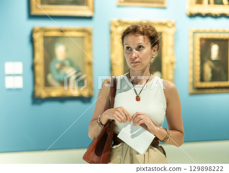Interested woman in casual clothes exploring paintings in halls of museum 129898222