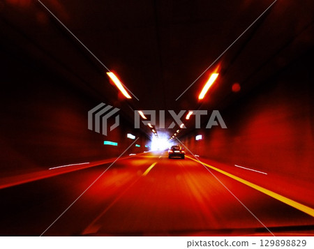 Car is driving down a tunnel with a red light on the tunnel wall 129898829
