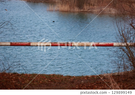 Red and white barrier is in the water next to a lake 129899149