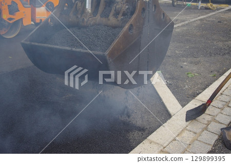 Black and grey construction vehicle is dumping gravel into a hole 129899395