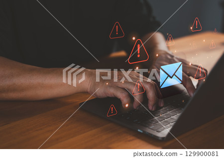 Person types on a laptop computer while warning email icons appear, symbolizing threats like phishing, malware, data breaches, scam messages, spam risks, and the need for cybersecurity protection. 129900081