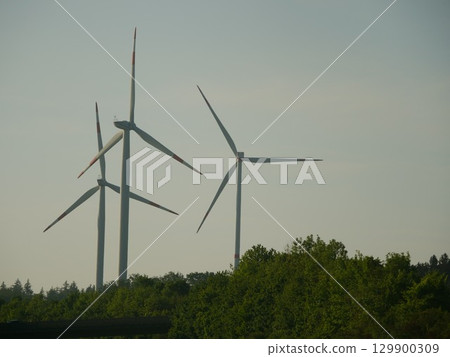 Three wind turbines are standing in a field with trees in the background Three wind turbines are standing in a field with trees in the background 129900309
